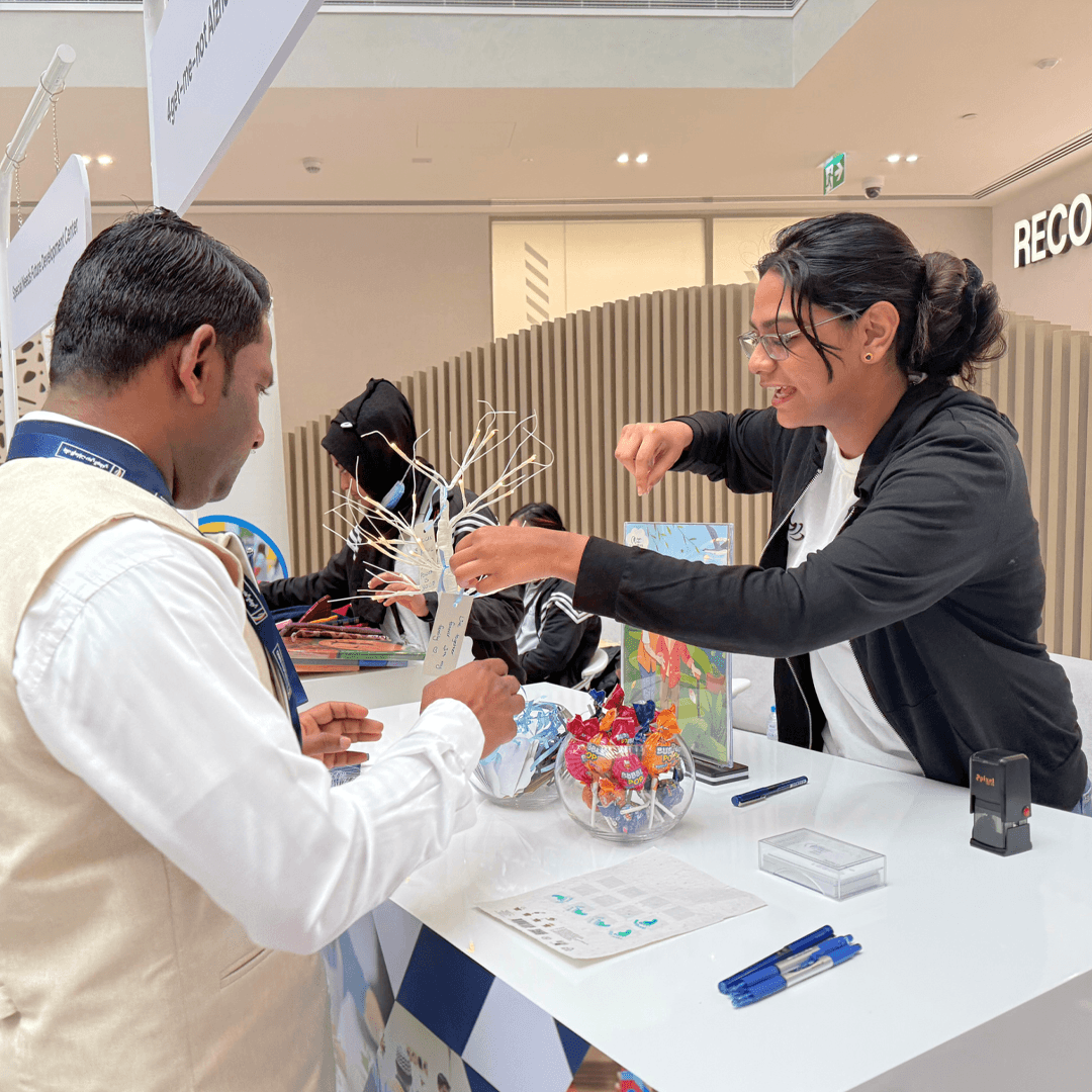 A Curtin Dubai student engaging with a senior citizen over a colourful Lego building activity during a 4get-me-not community event.