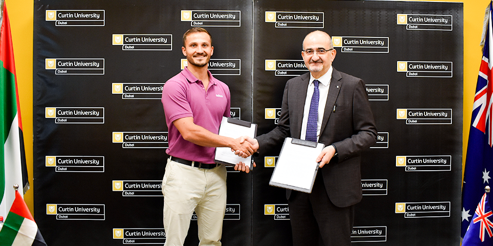 Representatives from Curtin University Dubai and Odoo smiling and holding the signed Memorandum of Understanding (MoU) document during the official partnership ceremony.