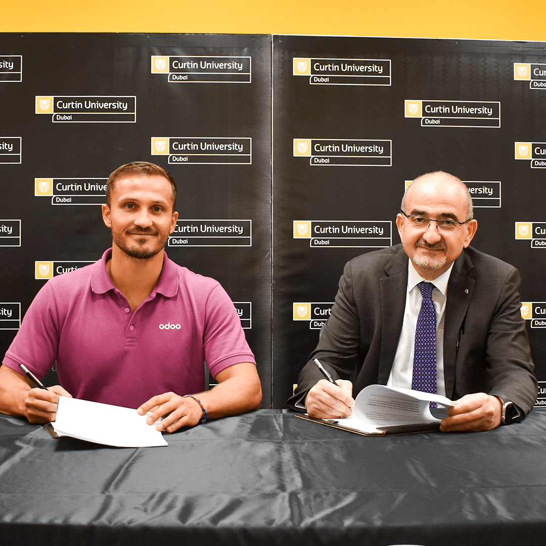 Representative from Odoo and Curtin University Dubai's Pro Vice-Chancellor and President smiling as they sign official partnership documents at a table during the MoU ceremony.